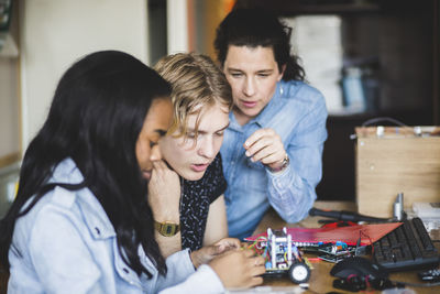 Teacher looking while confident students preparing toy car on desk in classroom