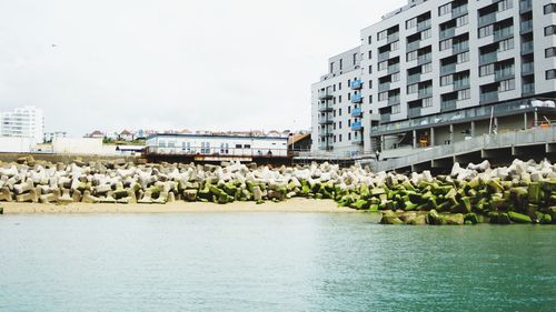 Buildings by river against sky in city