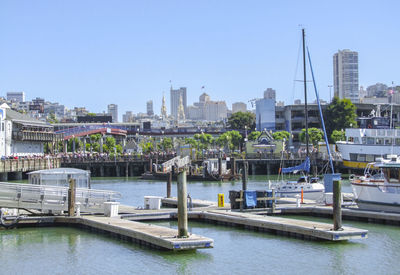 Boats in harbor by buildings against clear sky