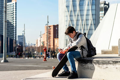 Young backpacker teenager sitting outdoors while using a smartphone