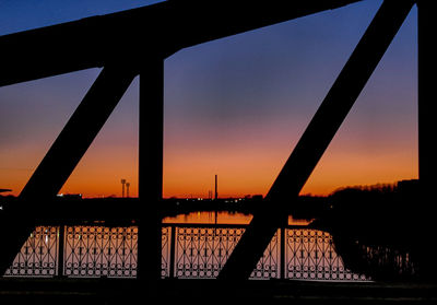 Silhouette bridge over river against sky during sunset