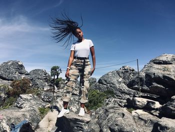 Low angle view of woman tossing hair while standing on rock