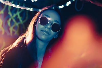 Portrait of confident young woman with illuminated reflection on sunglasses in restaurant