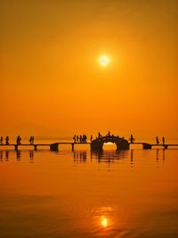 Silhouette people walking on pier over lake during sunset