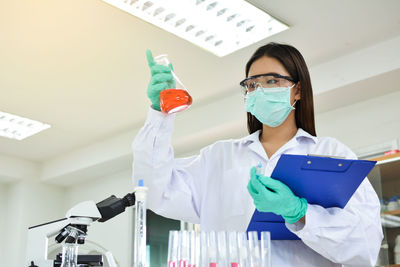 Female scientist with clipboard holding flask at laboratory