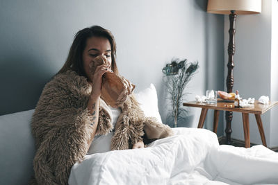 Young woman breathing in paper bag on bed at home