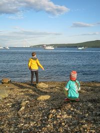 Rear view of siblings sitting on beach against sky