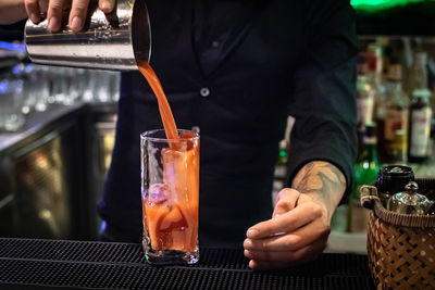 A bartender preparing and pouring a tasty bloody mary tomato juice alcoholic cocktail