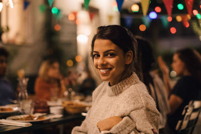 Portrait of smiling young woman sitting at table during dinner party in backyard