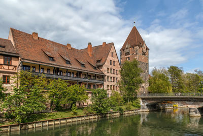 Arch bridge over river by buildings against sky