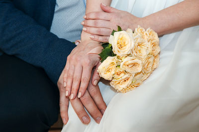 Midsection of couple holding hands while sitting with bouquet