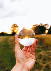 Cropped hand holding crystal ball on field against sky