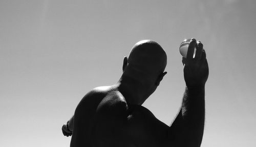 Rear view of bald man throwing crystal ball against clear sky