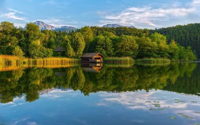 Reflection of house and trees in lake against sky