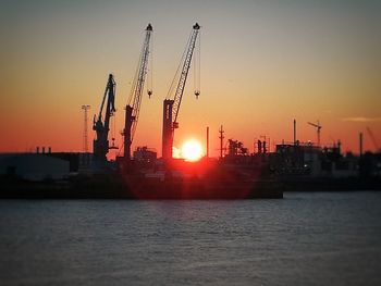 Cranes at commercial dock against sky during sunset