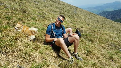 Full length of man sitting with dogs on mountain