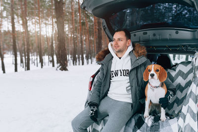 Man with dog sitting in car trunk