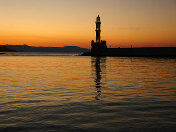 Lighthouse on pier in sea during sunset