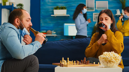 Man and woman playing chess while drinking beer at home