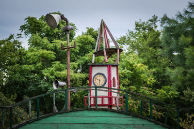 Low angle view of clock tower against trees on sunny day