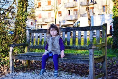 Full length of girl sitting on bench in city