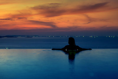 Rear view of silhouette woman in infinity pool against sea during sunset