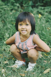 Portrait of cute girl crouching on grassy field