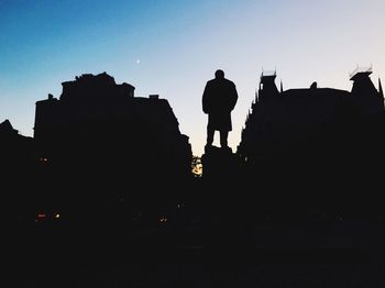 Low angle view of silhouette man standing by buildings against sky