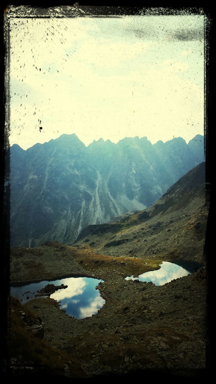 transfer print, mountain, auto post production filter, tranquil scene, tranquility, mountain range, scenics, landscape, beauty in nature, water, nature, sky, non-urban scene, lake, rock - object, idyllic, remote, outdoors, day, reflection