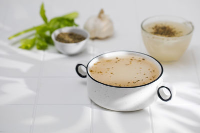 Healthy bone broth with spices in minsk on a white tile with a shadow pattern. 
