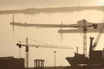 Cranes at harbor against sky