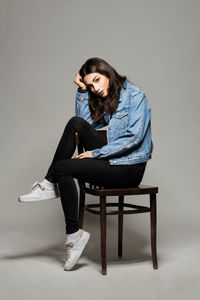 Young woman sitting on chair against wall