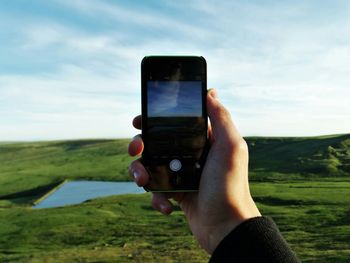 Cropped hand photographing green landscape with smart phone