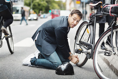 Businessman looking away while repairing bicycle on street