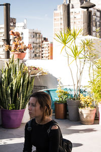 Portrait of young woman standing by potted plants