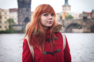 Portrait of young woman standing against river in city