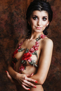 Portrait of shirtless young woman with floral decoration standing against wall