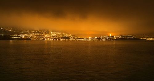 Illuminated city by sea against sky at night