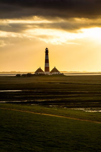 Lighthouse on field against cloudy sky