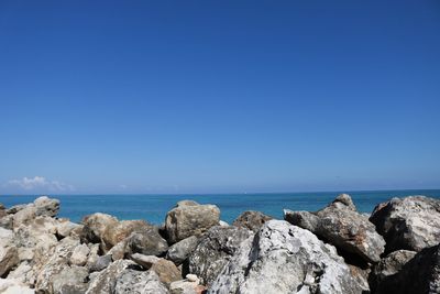 Rocks by sea against clear blue sky