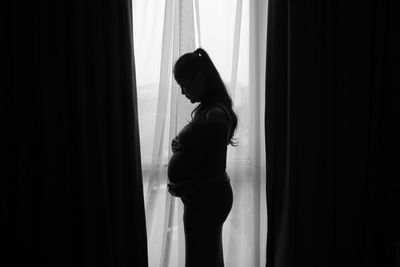 Side view of woman standing against curtain at home