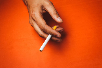 Cropped hand holding cigarette against orange background