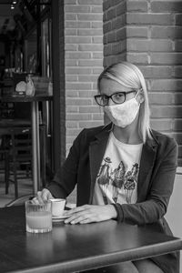 Portrait of young woman with mask sitting at cafe and restaurant table