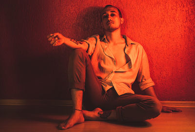 Portrait of young man sitting against wall