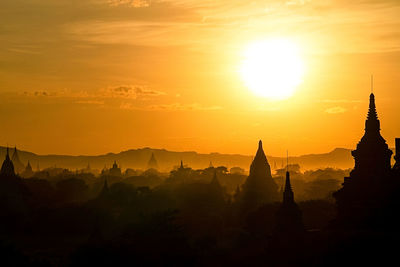 Silhouette temple against building during sunset