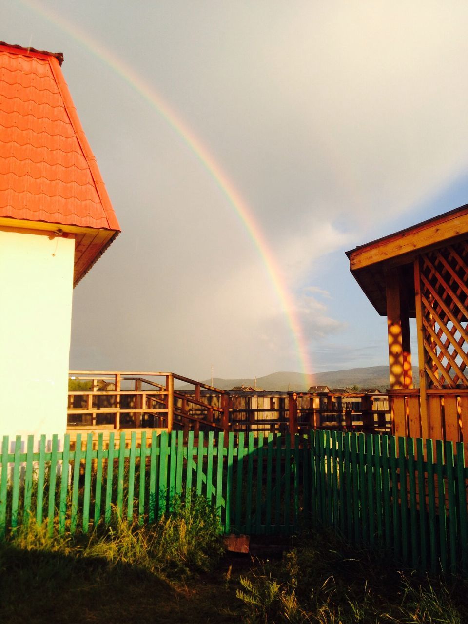 architecture, built structure, sky, rainbow, building exterior, multi colored, cloud - sky, house, cloudy, nature, fence, outdoors, cloud, weather, beauty in nature, railing, residential structure, no people, field, scenics