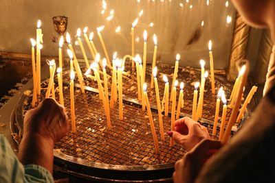 Cropped image of hands placing illuminated candles on metal grate at church