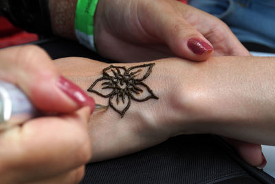 Cropped hand of artist applying henna tattoo on human hand