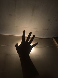 Low angle view of silhouette hand against illuminated wall