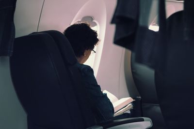 Woman reading book while sitting in airplane